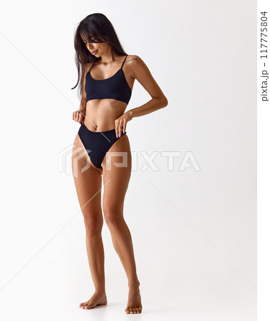 Full length photo of young fit woman dressed black inner wear posing shows her toned figure against white studio background. Full length photo of young fit woman dressed black inner wear posing shows her toned figure against white studio background. 117775804