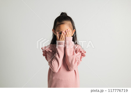 Asian portrait young kid girl in depressed bad mood covering face with hands and peering out with one eye between fingers studio isolated on white background, kindergarten child surprised and shocked Asian portrait young kid girl in depressed bad mood covering face with hands and peering out with one eye between fingers studio isolated on white background, kindergarten child surprised and shocked 117776719