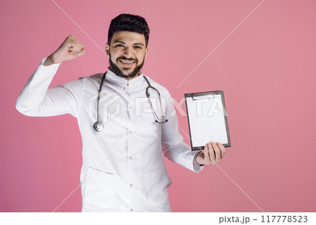 Front view of handsome doctor wearing medical gown, standing, looking at camera, smiling, showing folder. Concept of medicine. 117778523