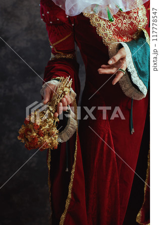 Closeup on medieval queen in red dress with dried flower Closeup on medieval queen in red dress with dried flower 117778547
