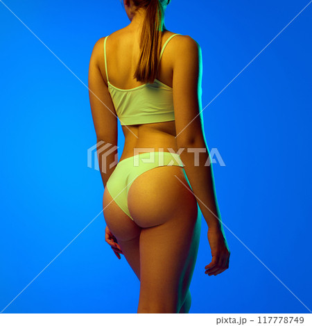 Cropped image of fit, smooth, healthy female body, buttocks in underwear against blue studio background in neon light. Anti-cellulite care Cropped image of fit, smooth, healthy female body, buttocks in underwear against blue studio background in neon light. Anti-cellulite care 117778749