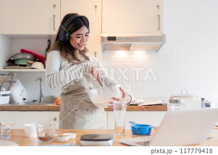 Happy Home Baker Mixing Ingredients with Laptop Nearby Happy Home Baker Mixing Ingredients with Laptop Nearby 117779418