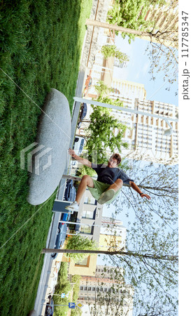 Jumping over large stone, young sportive man showing athletic agility,performing dynamic moves during parkour training in public park 117785347