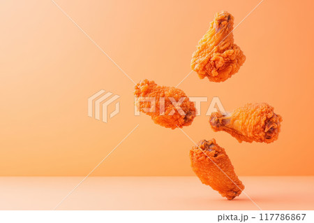 Delicious fried chicken wing floating against an orange background, showcasing golden crispy texture and mouth-watering appeal. 117786867