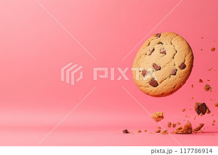 A delicious chocolate chip cookie floating mid-air with crumbs against a vibrant pink background. Ideal for food-themed projects. 117786914