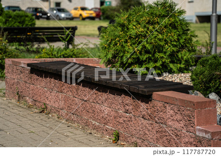 An outdoor, wooden bench without a back is mounted on a high curb An outdoor, wooden bench without a back is mounted on a high curb 117787720