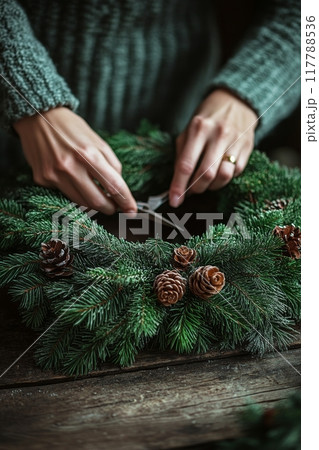Person crafting a holiday wreath using greenery and scissors in a cozy indoor setting 117788536