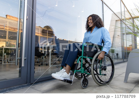 Dark-skinned young smiling disabled woman in a wheelchair near the office building 117788709