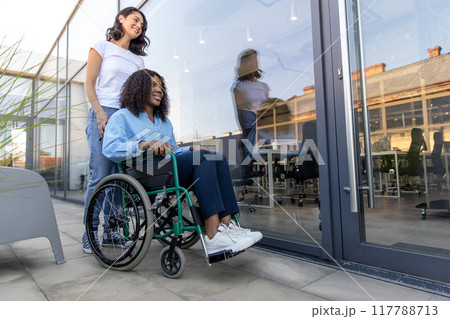 Young woman carrying a wheelchair with a disabled african american woman Young woman carrying a wheelchair with a disabled african american woman 117788713