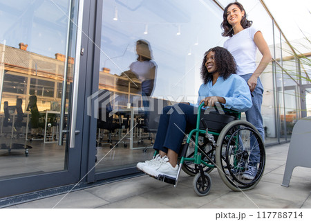 Young woman carrying a wheelchair with a disabled african american woman 117788714