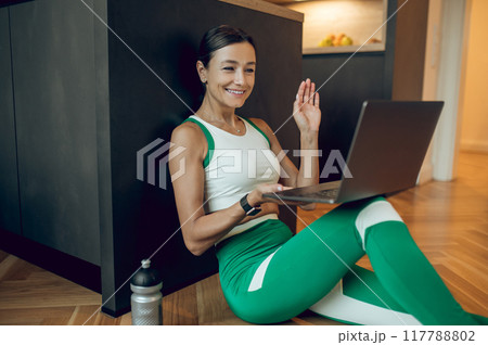 Female fitness coach having online class talking with her client via laptop in home interior Female fitness coach having online class talking with her client via laptop in home interior 117788802