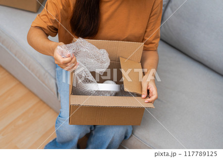 On her sofa, a cheerful lady unboxes a parcel, revealing new headphones, relishing her successful online shopping adventure. On her sofa, a cheerful lady unboxes a parcel, revealing new headphones, relishing her successful online shopping adventure. 117789125