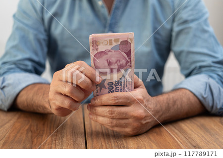 Man holding a stack of Turkish lira banknotes on a wooden table. Economic concept illustrating inflation and finance in Turkey. Man holding a stack of Turkish lira banknotes on a wooden table. Economic concept illustrating inflation and finance in Turkey. 117789171