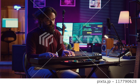 Sound engineer playing electronic piano keyboard and recording sounds, using mixing console and daw software to create new tunes. Music industry specialist uses stereo tools at home studio. Camera A. 117790628