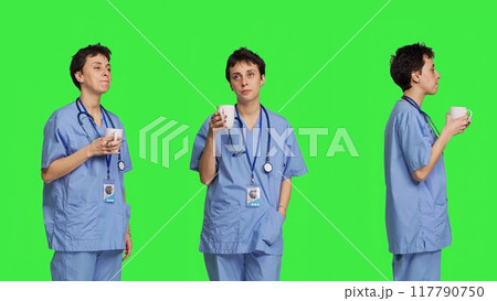 Medical assistant drinking cup of coffee before starting exam appointments in the morning, enjoying caffeine refreshment against greenscreen backdrop. Nurse drinks beverage. Camera B. 117790750