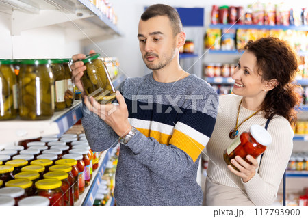 In Russian goods store, married couple choose jar of pickled tomatoes and cucumbers 117793900