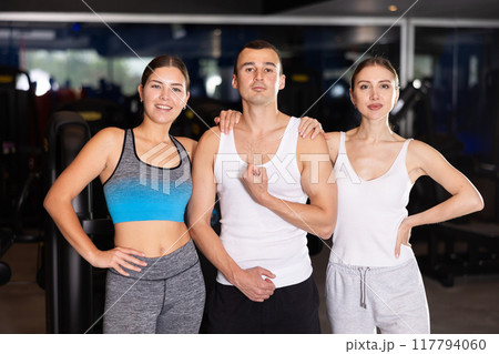 Positive young man and two girls posing together in gym Positive young man and two girls posing together in gym 117794060