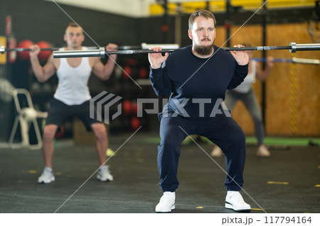 Young bearded man doing squats with barbell bar at intense training Young bearded man doing squats with barbell bar at intense training 117794164