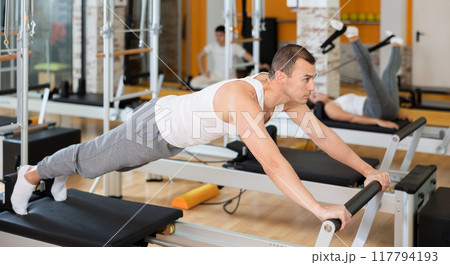 Man in different poses performs static and dynamic exercises on reformer Man in different poses performs static and dynamic exercises on reformer 117794193