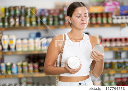 Girl is shopping in grocery department of supermarket - choosing canned goods 117794258
