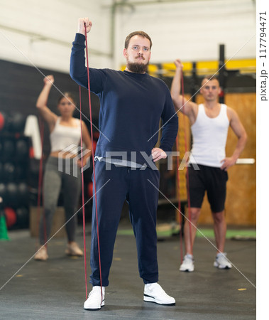 Determined young guy working out with resistance band in gym 117794471