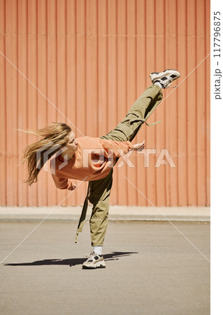 Dancer captured mid-air while performing dynamic move with hair flowing, against bright orange wall background with clear blue sky suggesting energetic and expressive dance style 117796875