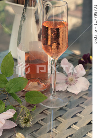 Rose wine and flowers on terrace on sunny day. Drinks of Mediterranean. Wicker furniture in garden, summer and vacation.  117798731
