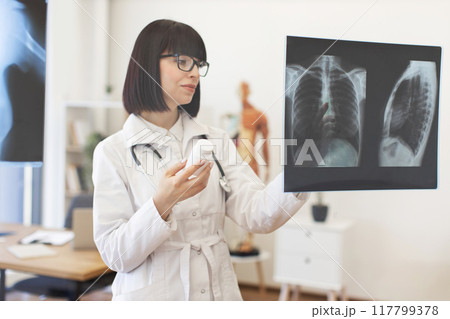 Female doctor analyzing x-rays while holding medicine bottle Female doctor analyzing x-rays while holding medicine bottle 117799378