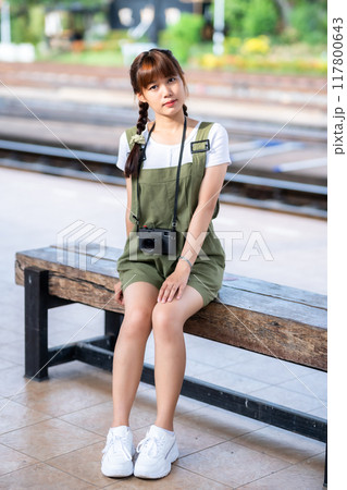Portrait Young asian woman smiling tourist Traveler girl walking and with a holding the camera waits train travel journey is taken in railway platform Thailand, summer relax vacation Concept. 117800643