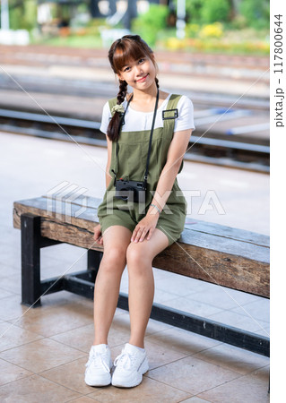 Portrait Young asian woman smiling tourist Traveler girl walking and with a holding the camera waits train travel journey is taken in railway platform Thailand, summer relax vacation Concept. 117800644