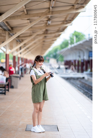 Portrait Young asian woman smiling tourist Traveler girl walking and with a holding the camera waits train travel journey is taken in railway platform Thailand, summer relax vacation Concept. 117800645