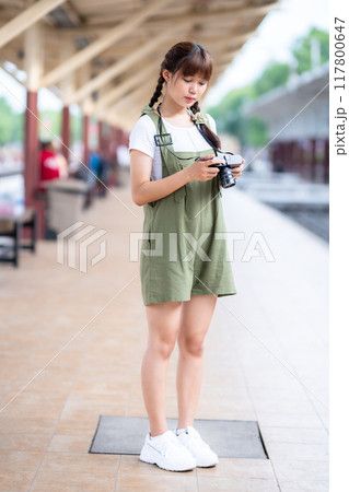 Portrait Young asian woman smiling tourist Traveler girl walking and with a holding the camera waits train travel journey is taken in railway platform Thailand, summer relax vacation Concept. 117800647