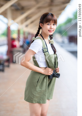 Portrait Young asian woman smiling tourist Traveler girl walking and with a holding the camera waits train travel journey is taken in railway platform Thailand, summer relax vacation Concept. 117800649