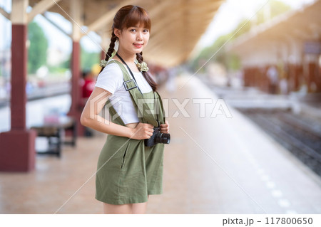 Portrait Young asian woman smiling tourist Traveler girl walking and with a holding the camera waits train travel journey is taken in railway platform Thailand, summer relax vacation Concept. 117800650