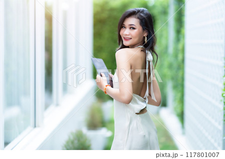 beautiful asian freelance Success people business woman fashion model in summer white sleeveless dress using casual working with tablet for browsing internet, chatting and blogging in coffee shop. 117801007