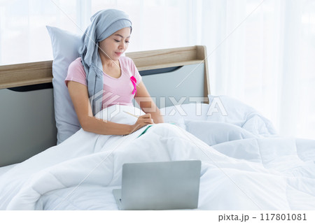 a asian women disease mammary cancer patient with pink ribbon wearing headscarf After treatment to chemotherapy with Take notes in a notebook and laptop on bed In the bedroom at the house,healthcare a asian women disease mammary cancer patient with pink ribbon wearing headscarf After treatment to chemotherapy with Take notes in a notebook and laptop on bed In the bedroom at the house,healthcare 117801081