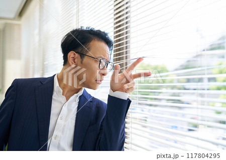 ブラインド越しに外を見つめる男性 117804295