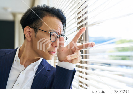 ブラインド越しに外を見つめる男性 117804296