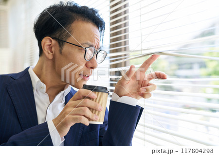 ブラインド越しに外を見つめる男性 117804298