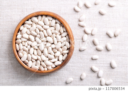 White beans in a wooden bowl on linen fabric. Dried small seeds, a variety of Phaseolus vulgaris, the common bean, a member of the legume family Fabaceae. Vegetarian staple food. Close up, from above. White beans in a wooden bowl on linen fabric. Dried small seeds, a variety of Phaseolus vulgaris, the common bean, a member of the legume family Fabaceae. Vegetarian staple food. Close up, from above. 117806534