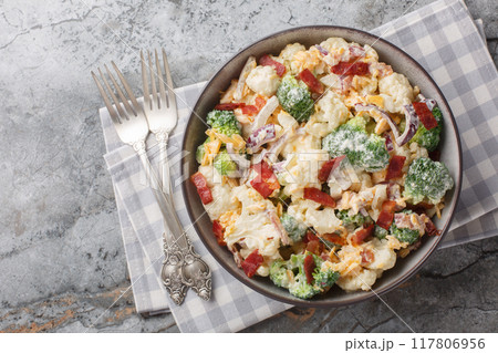 Delicious mayonnaise salad with broccoli, cauliflower, bacon, cheddar cheese and red onion close-up in a bowl on the table. Horizontal top view 117806956