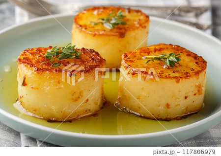 Deliciously cooked fondant melting potatoes are oven-braised in a buttery, thyme-flavored sauce closeup on the plate. Horizontal 117806979
