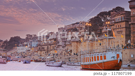 Varanasi, India. General View From Pleasure Boat on Chausathi Ghat. Purple Sunset Sky At Evening . Many Boats Moored On Ganga River. Devotees Take A Holy Dip In Water From This Ghat Varanasi, India. General View From Pleasure Boat on Chausathi Ghat. Purple Sunset Sky At Evening . Many Boats Moored On Ganga River. Devotees Take A Holy Dip In Water From This Ghat 117807199