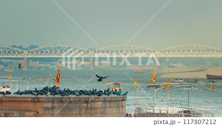 Varanasi, India. Bird Take Off from Sacred Ghat In Varanasi. Pigeons Fly Up In Slow Mo. Birds Flight. Orange Flags Fluttering In Slow Mo, Symbolizing Hanuman. Cinematic View On Ganga River. Many 117807212