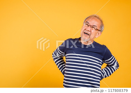 Portrait Asian old man with glasses holds hands on back he backache studio shot isolated yellow background, senior man pensioner suffering of backache, problems muscular pain 117808379