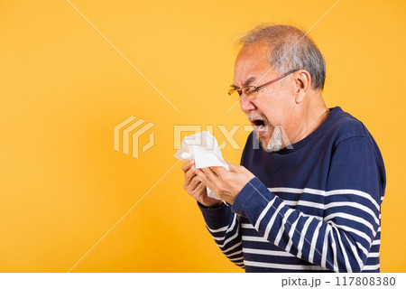 Asian elder man cold having flu and sneezing from sickness virus problem use tissue studio shot isolated on yellow background, Portrait senior old man blowing nose with tissue, pensioner unwell 117808380