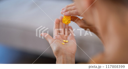 Elderly Woman Pouring Pills from Bottle for Daily Medication 117808399