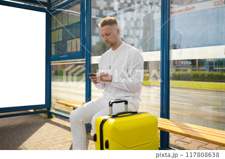 Handsome Tourist Caucasian business man traveler with bag and suitcase sit at public transport bus station waiting with mobile smart phone Handsome Tourist Caucasian business man traveler with bag and suitcase sit at public transport bus station waiting with mobile smart phone 117808638
