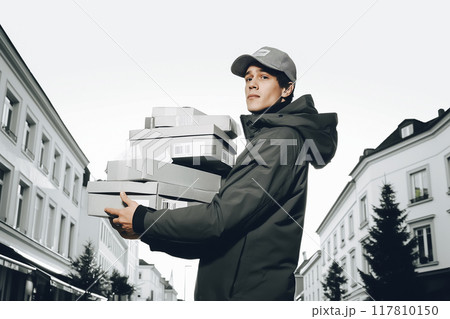 Confident young delivery man carrying cardboard boxes. Confident young delivery man carrying cardboard boxes. 117810150