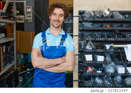 Portrait of workman in repair shop garage standing at rack with supplies 117811547